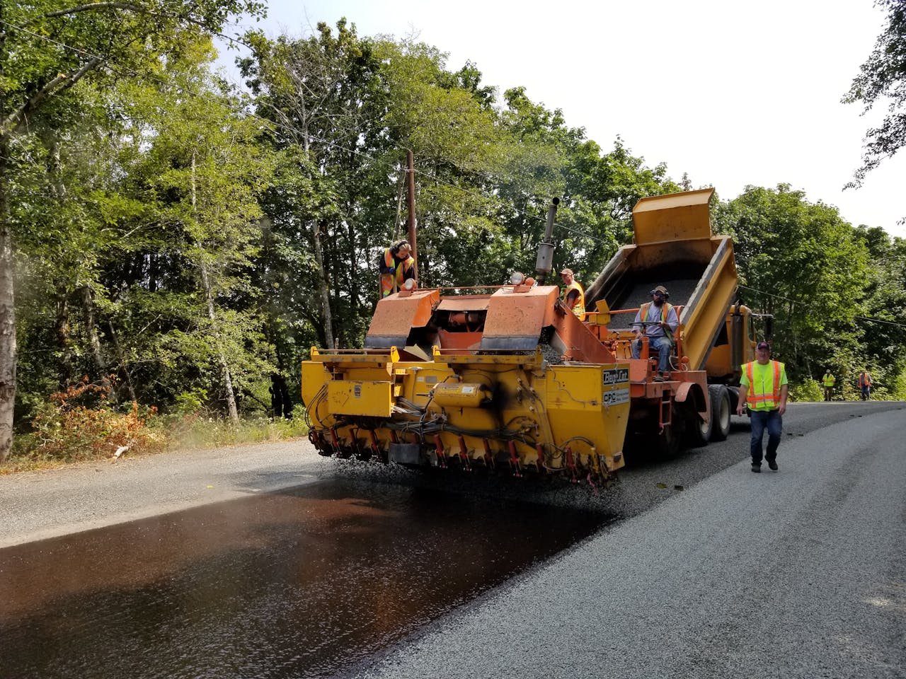 About Road paving in Oregon forest with workers and machinery. Summer construction scene outdoors.